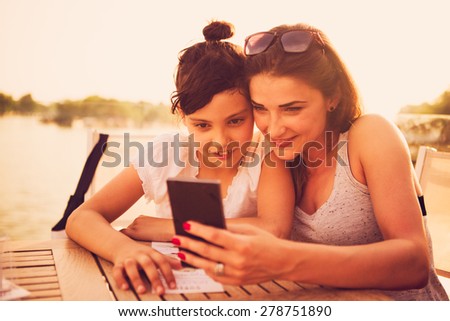 Mother and daughter sitting at cafe and looking at smart phone