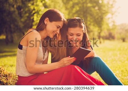 Two girls in the park watching funny video on the tablet