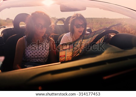 Two young women in cabriolet traveling and looking at the map