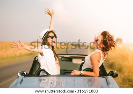 Two happy female friends enjoying road trip in their cabriolet