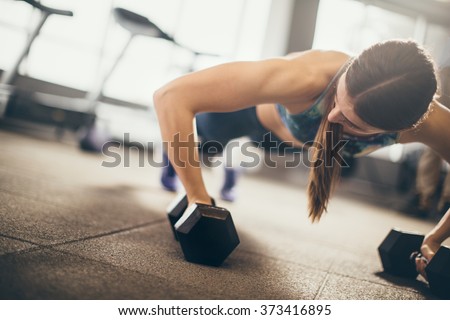 Woman doing push-up exercise with dumbbell. Strong female doing crossfit workout.