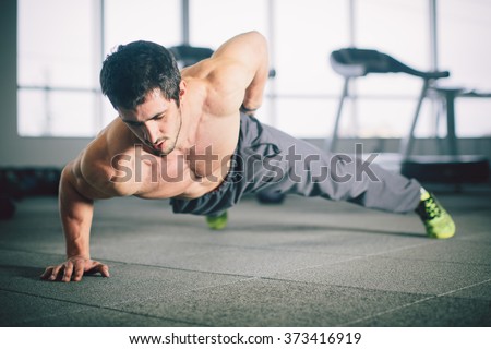 Portrait of a handsome man doing push ups exercise with one hand in fitness gym