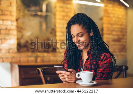 Young african woman at cafe drinking coffee and using mobile phone
