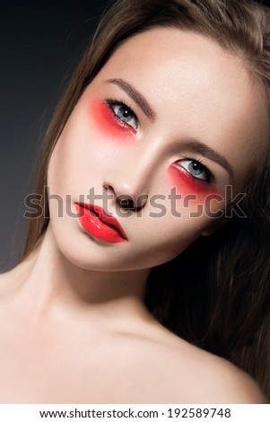 Beautiful girl with bright creative makeup. Red lips, perfect skin. Portrait shot in the studio on a black background.