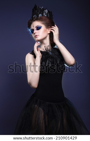 Gothic girl with a crown and a necklace of feathers and creative makeup. Picture taken in the studio
