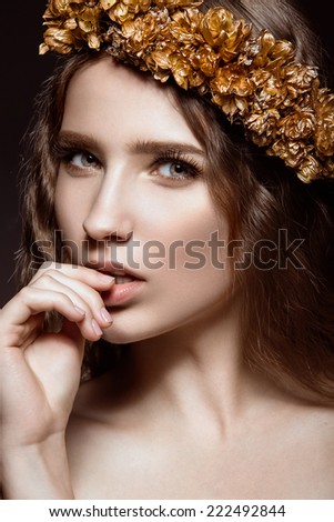 Beautiful girl with golden makeup and autumn wreath in her hair. Beauty face. Portrait shot in the studio on a black background.