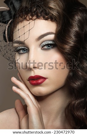 Beautiful woman with evening make-up, red lips and curls. Beauty face. Picture taken in the studio on a gray background.