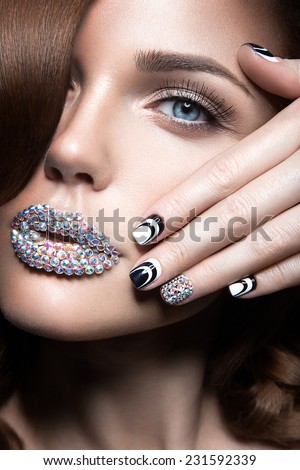 Beautiful girl with bright nails and lips of crystals, long eyelashes and curls. Beauty face. Picture taken in a studio.