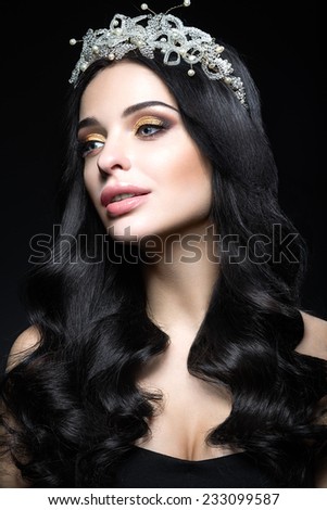 Beautiful dark-haired woman with a crown of precious stones, curls and evening makeup. Beauty face. Picture taken in the studio on a black background.