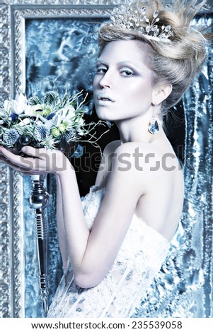 Beautiful girl in white dress in the image of the Snow Queen with a crown on her head. Picture taken in the studio with decorations.