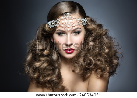 Beautiful woman with evening make-up and curls and big jewelry on her head. Beauty face. Picture taken in the studio on a gray background.
