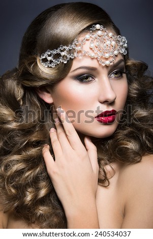 Beautiful woman with evening make-up and curls and big jewelry on her head. Beauty face. Picture taken in the studio on a gray background.