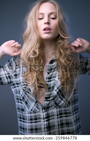 Beautiful blonde girl in a plaid shirt with a light make-up and loose hair. Model tests. Picture taken in the studio on a gray background.