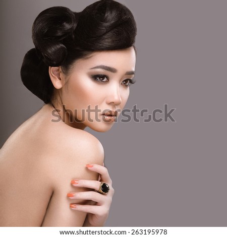 Beautiful girl with oriental type evening hair and makeup. Beauty face. Portrait shot in the studio on a gray background.