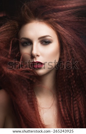Beautiful girl with bright makeup and burgundy lips with the wind in hair. Beauty face. Picture taken in the studio on a black background.