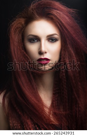 Beautiful girl with bright makeup and burgundy lips with the wind in hair. Beauty face. Picture taken in the studio on a black background.