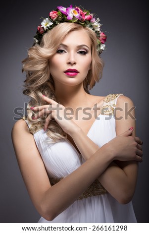 Beautiful blond girl in the image of a bride with flowers in her hair. Picture taken in the studio on a grey background. Beauty face