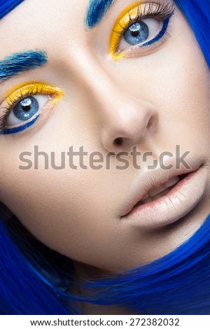 Beautiful girl in a bright blue wig in the style of cosplay and creative makeup. Beauty face. Art image. Picture taken in the studio on a yellow background.