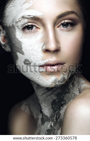 Beautiful girl with mud on his face. Cosmetic mask. Beauty face. Picture taken in the studio on a black background.