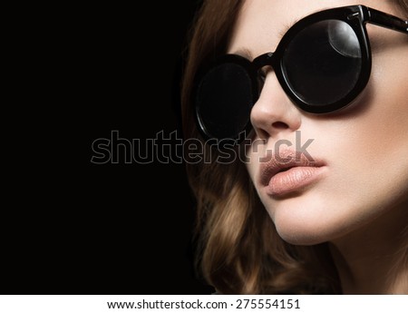 Beautiful girl in dark sunglasses, with curls and evening makeup. Beauty face. Picture taken in the studio on a black background.