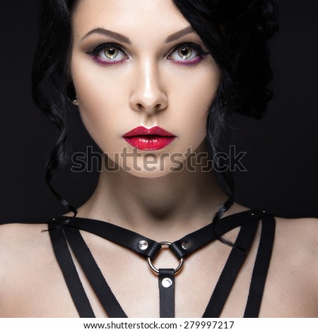 Beautiful Girl in the Gothic style with leather accessories and bright makeup. Beauty face. Picture taken in the studio on a black background.