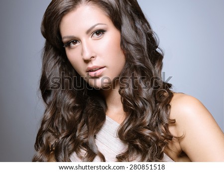 Beautiful woman in a light dress with evening makeup, pale lips and curls. Beauty face. Picture taken in the studio on a gray background.