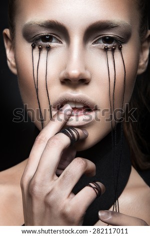 Beautiful girl with creative make-up in Gothic style and the threads of eyes. Art beauty face. Picture taken in the studio on a black background.