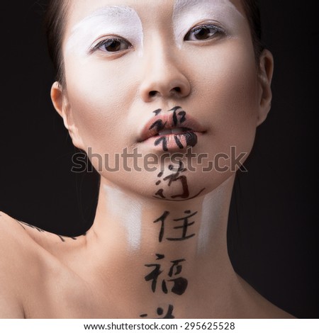 Beautiful Asian girl with white skin, red lips and hieroglyphics on her face. Art Beauty image.