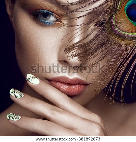 Beautiful girl with bright makeup, manicure design and peacock feather on her face. Art nails. Photos shot in the studio.