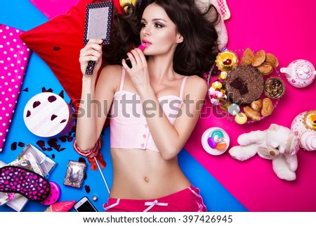 Beautiful fresh girl doll lying on bright backgrounds surrounded by sweets, cosmetics and gifts. Fashion beauty style.