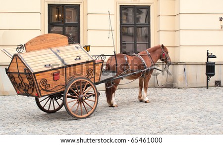 horse harnessed to a cart standing on the pavement outside the house