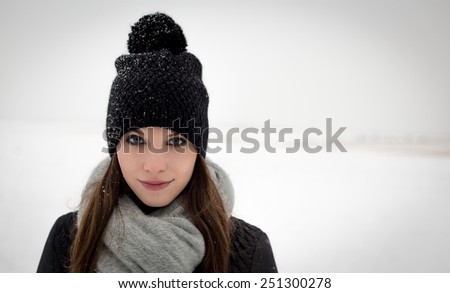 Outdoor portrait of a young girl in winter hat with pom-pom scarf and snowy plains in the background