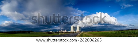 Nuclear plant and its cooling towers releasing a huge cloud of steam to the sky, verdant vegetation around