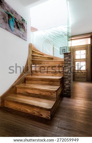 Wooden stairs with visible wood texture in bright daylight coming from the second floor. Stairs are lined with paneled stone wall and illuminated glass panel with a blue touch.