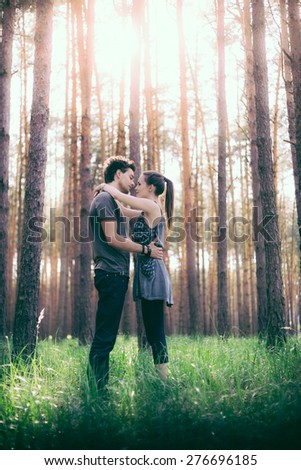 Man and woman in each other\'s arms in the environment of pine forest with grassy undergrowth in the glare of the morning sun.