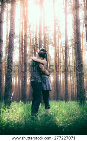 Man and woman in closed embrace of each other in the environment of pine forest with grassy undergrowth in the glare of the morning sun.