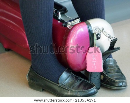 A school girl in uniform holds her instrument between her feet with a pink good luck charm for safety hanging from it.