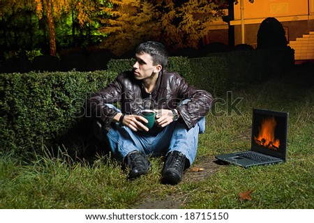 Conceptual picture about autumn, one young man with a cup of coffe seats near laptop which the fireplace role carries out, he thinks of summer, which for a long time already behind