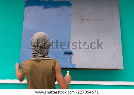 Young painting facade builder worker with roller at thermal insulation works
