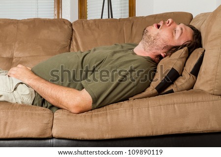 Fat obese man  on the couch with remote in one hand and the other hand shoved down the front of his pants. Shows obesity due to lack of exercise.