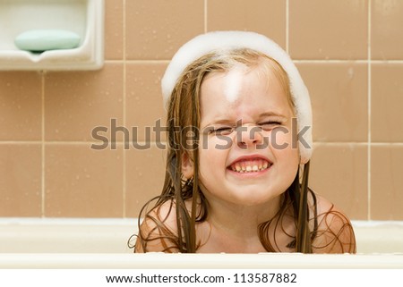 Playing in the tub making a weird funny face or smile, this cute girl is having fun.