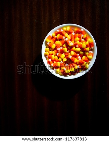 Top down view of candy corn on a dim lit wood table giving a creepy scary vibe