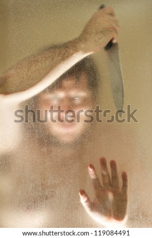 Man with a knife up against a shower door. Man\'s face is obscured mostly by the shower door