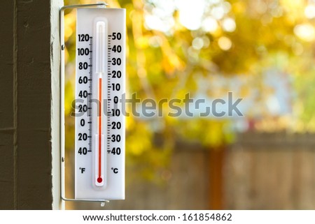 Image of a thermometer with pretty colors of fall in the background