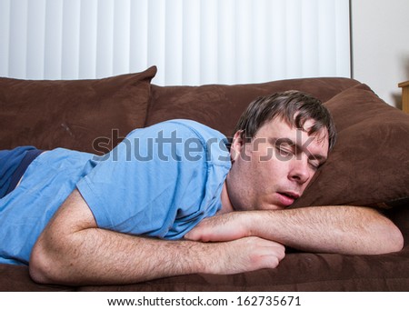 Guy passed out on couch with arms wrapped around a pillow