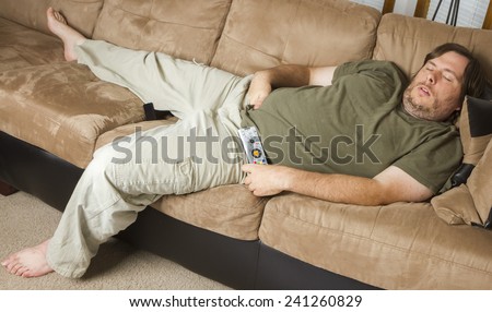 laying down on the couch with his hands down his pants a fat man is asleep