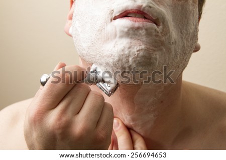 Shaving under his chin a man is getting clean for the day. He us using a double edged safety razor