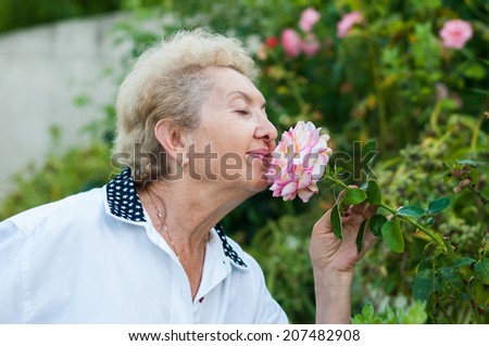 Nice elderly woman smelling flower in the garden on a warm summer day. Enjoying life after retirement. Lifestyle image of grandmother in the garden living a stress free life