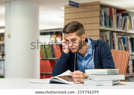 Bored male student reading books in the library. Studying for exam. Education concept