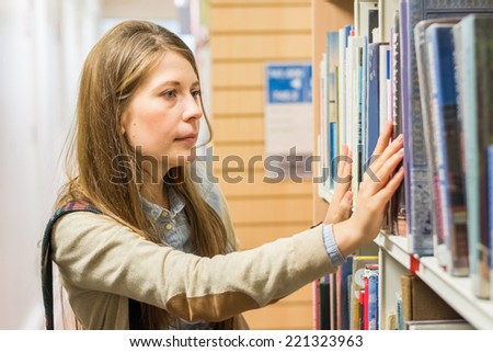 Attractive young woman university student searching for books in the library. Knowledge and education concept
